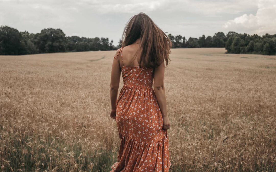 Femme en robe rouge à motifs, marchant dans un champs de blé